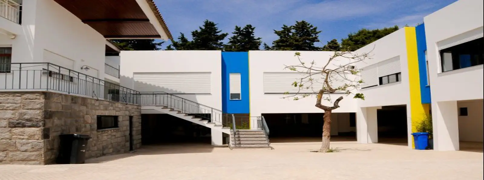 Courtyard and white classroom blocks with blue and yellow details at Colégio Quinta do Lago