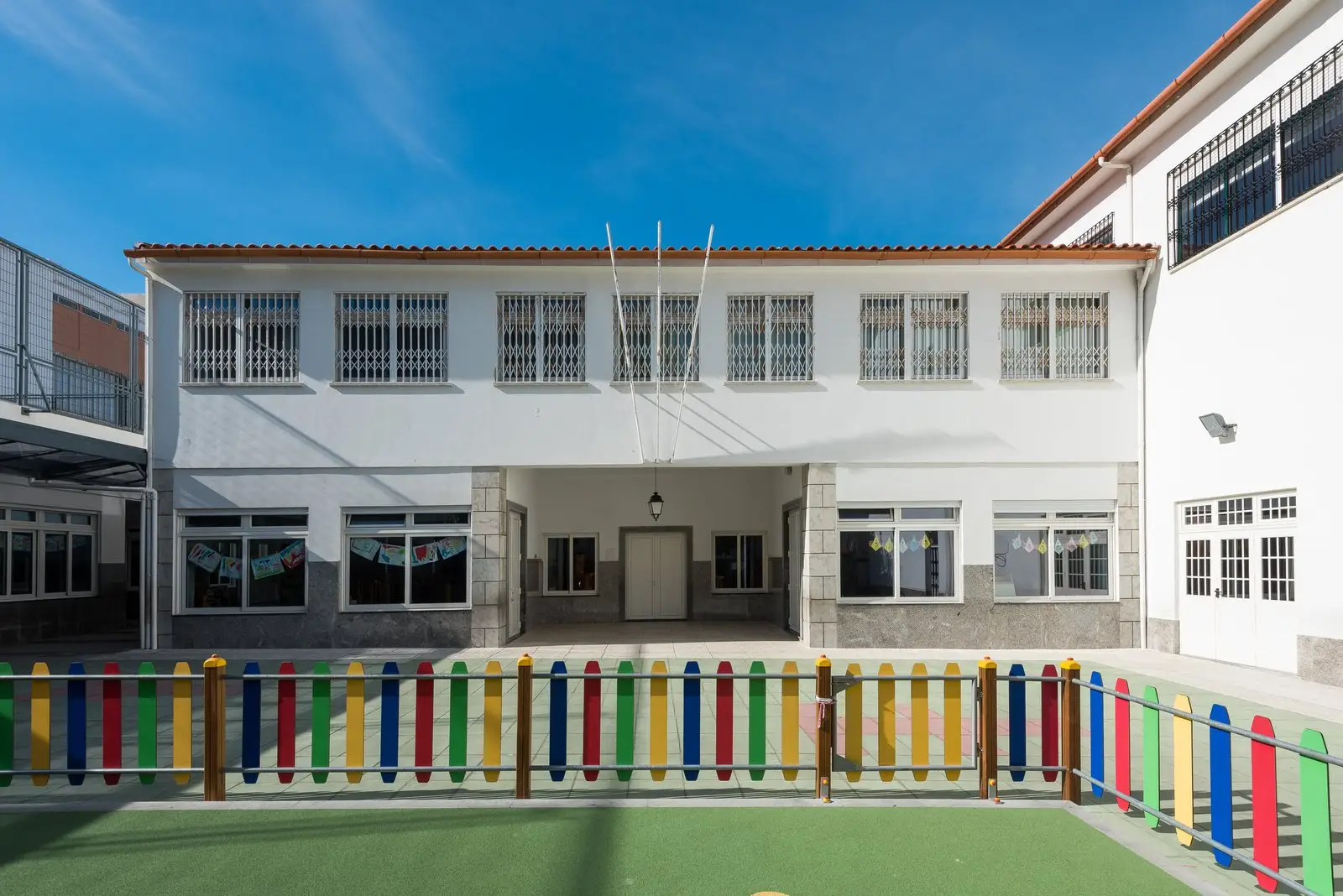 White school building behind a playground with a colourful fence at Externato Nossa Senhora da Assunção