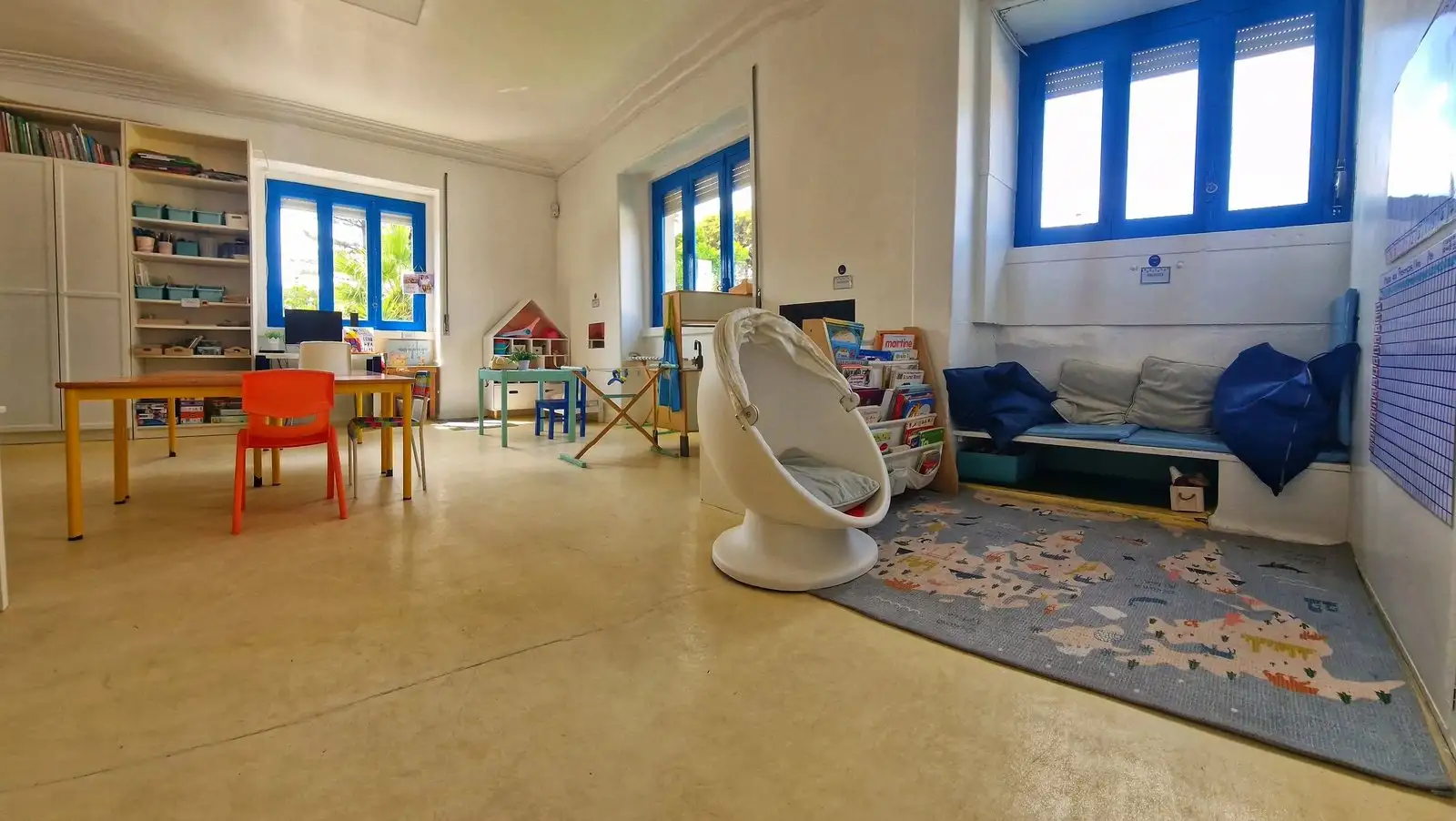 Bright classroom with blue windows, a reading corner and small tables at Colégio Príncipes de Aviz