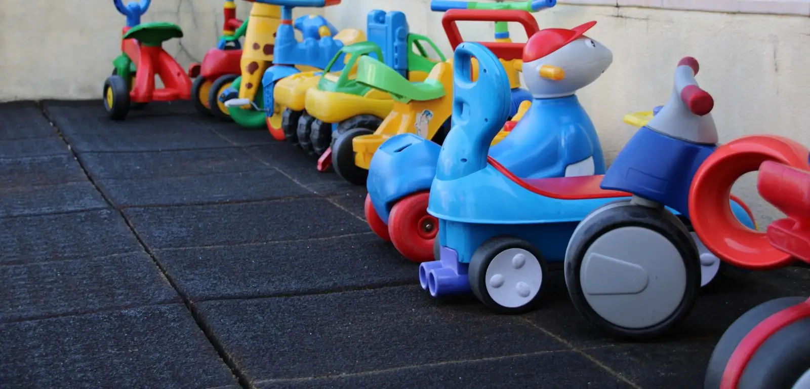 A row of children's ride-on toys and tricycles in the covered playground at Externato Florinda Leal