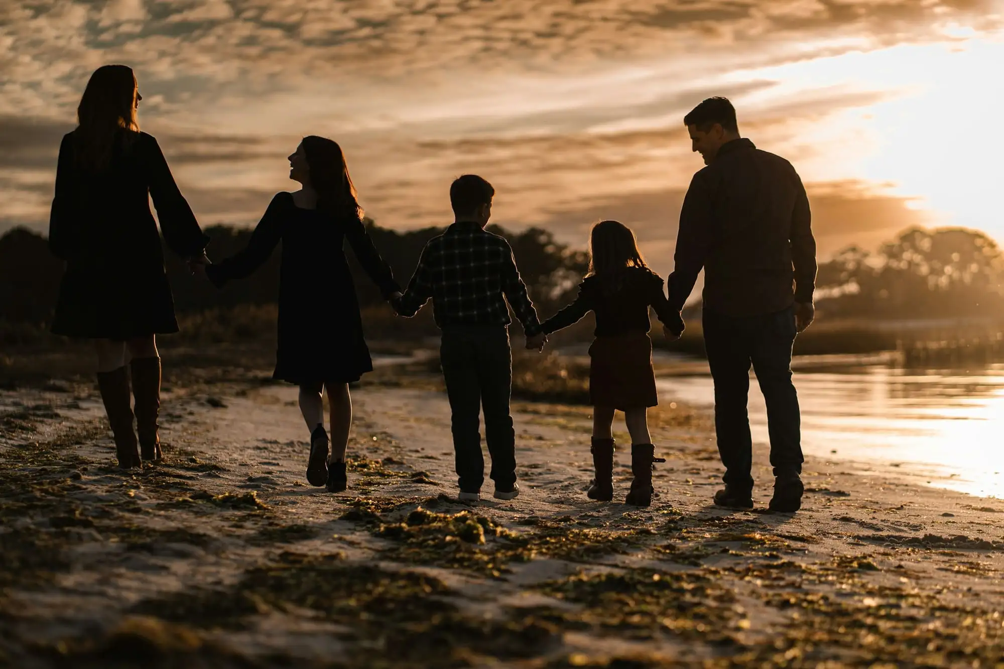 A family walking hand in hand along a beach at sunset, seen from behind